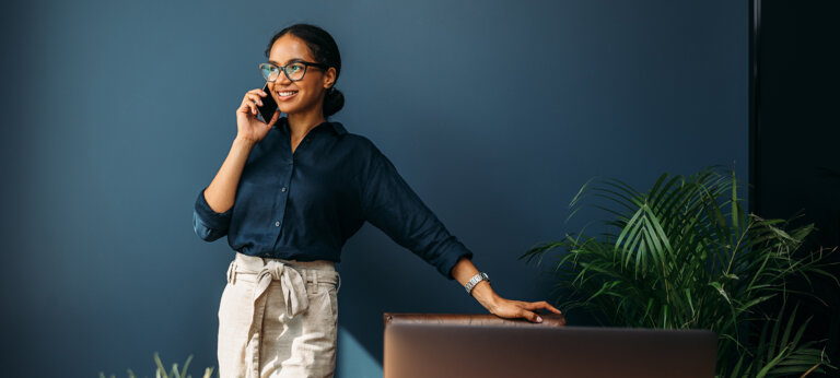 A well-dressed, smiling woman talking on the phone in a modern-looking office space