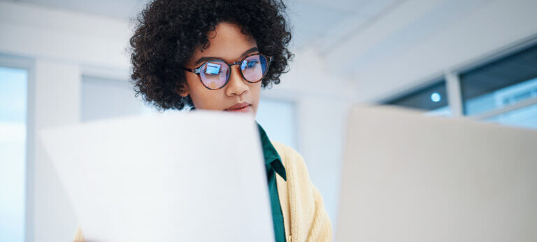 Woman holding a piece of paper and working on a laptop