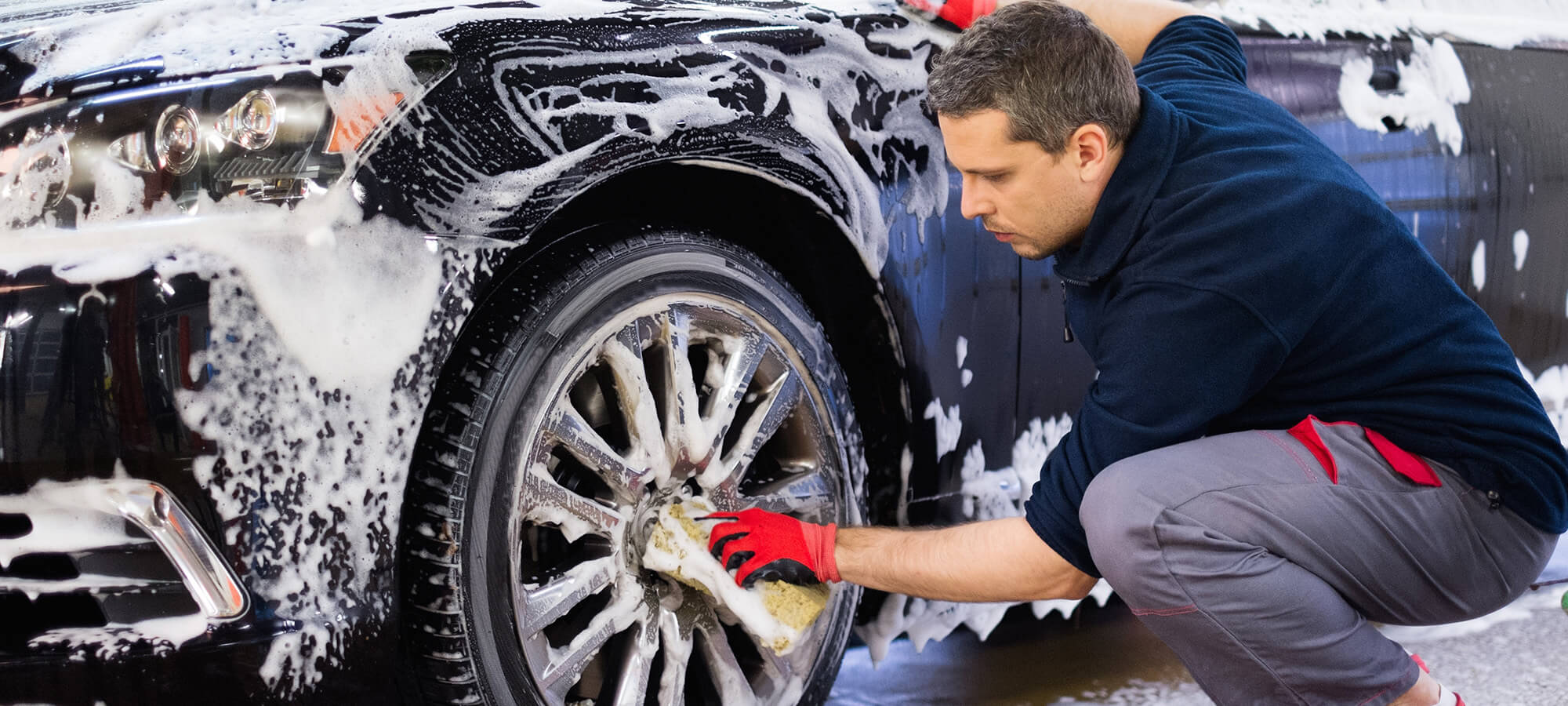 Man worker washing car's alloy wheels on a car wash