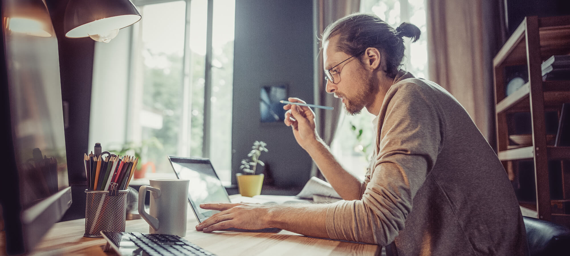 Young freelancer working with laptop at home. Side view of male working on freelance at home office.