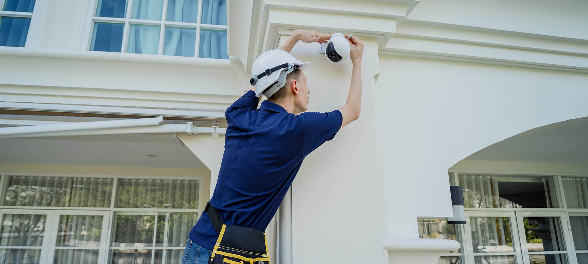 A technician installs a CCTV camera on the facade of a residential building.