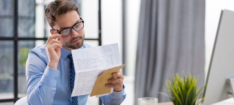 entrepreneur man reading an invoice from envelope in a desktop at office.