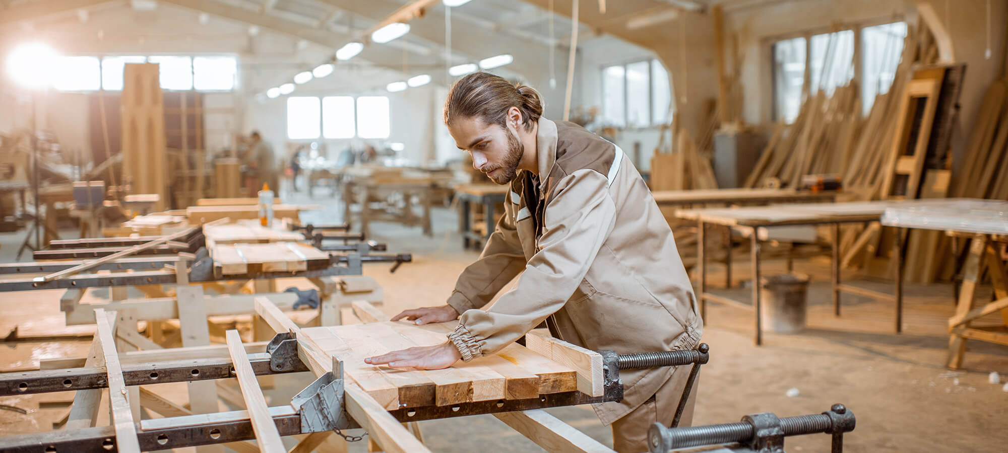 carpenter in uniform gluing wooden bars with hand pressures at the carpentry manufacturing