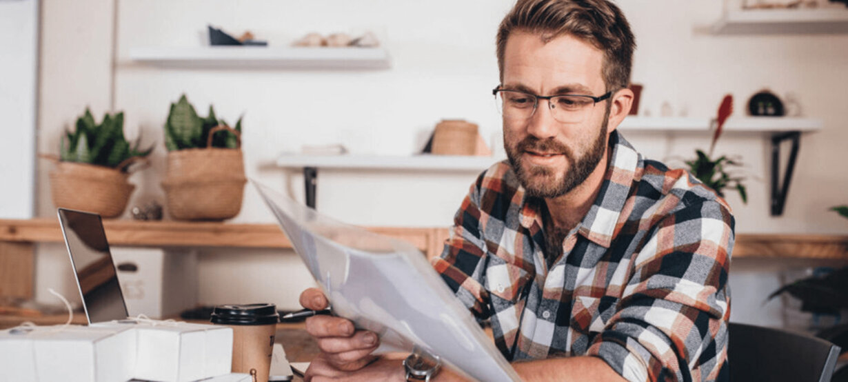 A smiling man with a laptop, looking at some papers